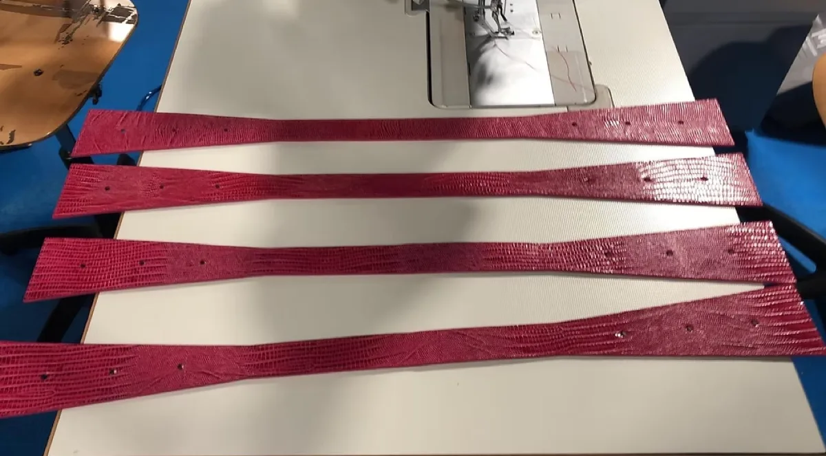 Cuatro tiras de piel grabada cortadas y perforadas, alineadas sobre la mesa de la máquina de coser